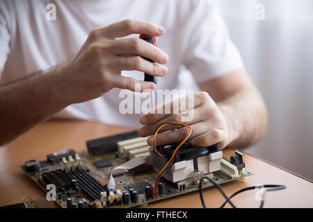 Close-up di mani del giovane ingegnere informatico di fissaggio pc rotto le parti presso la scrivania in ufficio in casa Foto Stock
