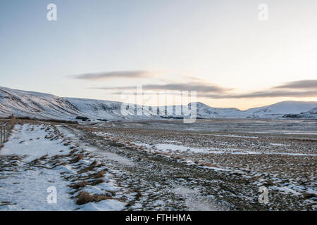 Coperta di neve campo circondato da montagne innevate con un cielo chiaro a sunrise in Islanda Foto Stock