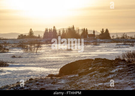 Thingvellir chiesa, Islanda attraverso il fiume ghiacciato con bassa giallo sole in inverno Foto Stock