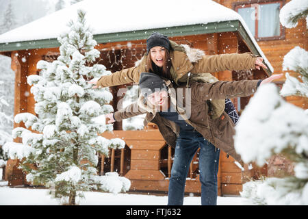 Allegro attraente uomo barbuto piggibacking la sua ragazza e divertirsi in inverno Foto Stock