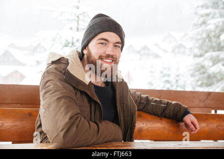 Allegro barbuto giovane uomo seduto all'esterno in inverno Foto Stock