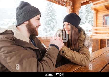 Felice coppia giovane seduti sulla terrazza presso il tavolo in legno e tenendo le mani in inverno Foto Stock