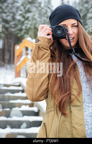 Allegro piuttosto giovane donna con capelli lunghi per scattare delle foto di voi su scale nella foresta di inverno Foto Stock