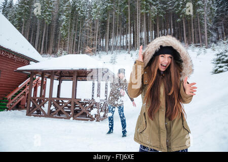 Felice eccitato coppia giovane gioca snowballs e urlando vicino alla casa nel bosco invernale Foto Stock