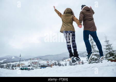 Vista posteriore della coppia giovane jumping e divertirsi insieme in inverno Foto Stock