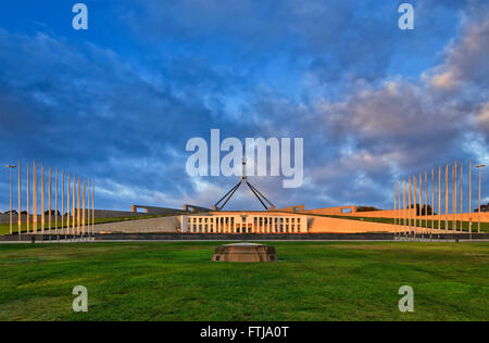 Prato verde e bandiera alti pali con bandiere nella parte anteriore del nuovo Parlamento a Canberra a sunrise. Territorio della Capitale Australiana Foto Stock