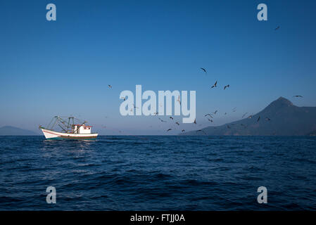 Una barca da pesca trascinando un gambero net off Ilhabela, se il Brasile. Uccelli come sule e frigatebirds sono i seguenti per ottenere il rottame Foto Stock