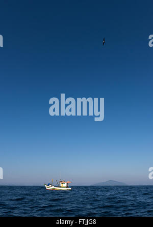Una barca da pesca trascinando un gambero net off Ilhabela, se il Brasile. Uccelli come sule e frigatebirds sono i seguenti per ottenere il rottame Foto Stock