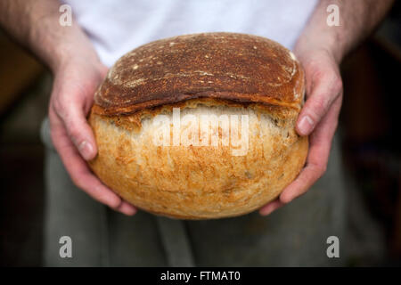 Un Baker detiene una pagnotta di pane appena sfornato soda il pane nelle sue mani Foto Stock