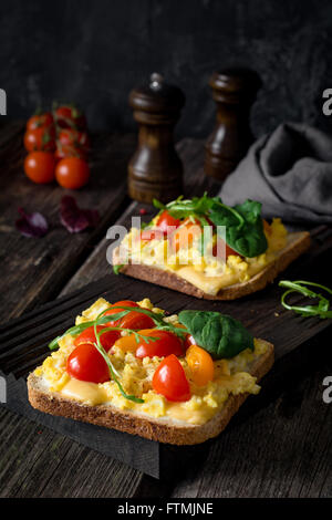 Toast per la prima colazione con uova strapazzate, formaggio, pomodori ciliegini, rucola e insalata di mais rustico sfondo di legno