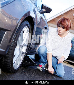 Donna sostituzione della ruota sulla sua automobile Foto Stock