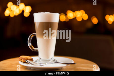 Caffe macchiato bevanda di caffè in un lungo il vetro è servita in una caffetteria su un piattino con un biscotto. Foto Stock