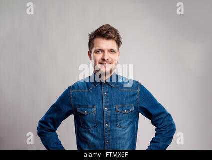 Uomo in camicia denim, braccia sui fianchi e sfondo grigio. Foto Stock