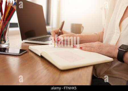Chiudere l immagine della donna seduta alla sua scrivania e scrivere le note. Imprenditrice lavora da casa in ufficio. Foto Stock