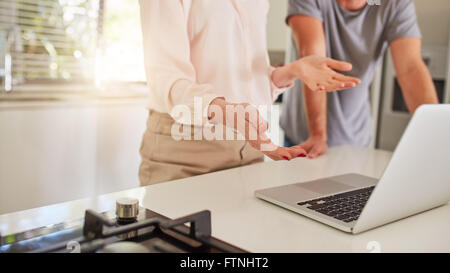 Ritagliato shot del giovane a lavorare insieme su un computer portatile in cucina. Matura in piedi dal banco di cucina, con la donna explainin Foto Stock