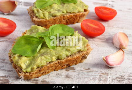 Ingredienti e panini freschi con pasta di avocado, pane di segale, pomodori ciliegini, aglio, basilico, il concetto di sano Foto Stock