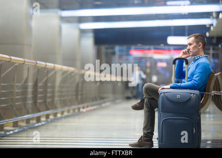 Ritratto di giovane bello per chi indossa uno stile informale vestiti seduta sul banco in aeroporto moderno terminale. Traveler Foto Stock