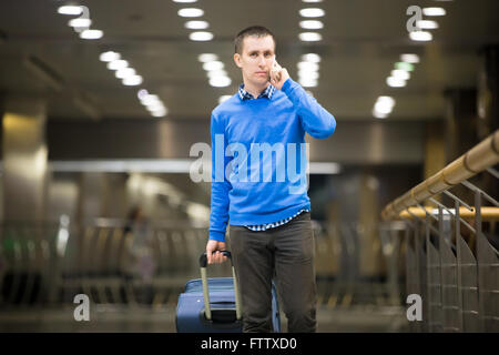 Ritratto di giovane bello ragazzo indossa uno stile informale vestiti a piedi nella stazione di moderno. Traveler di effettuazione della chiamata utilizza lo smartphone Foto Stock