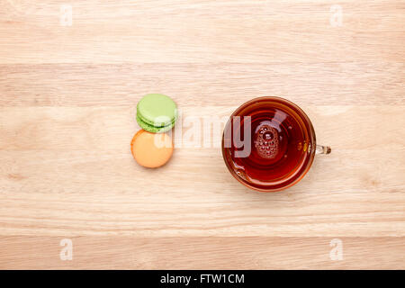 Bicchiere di vetro di tè nero e due macarons colorati su sfondo di legno Foto Stock