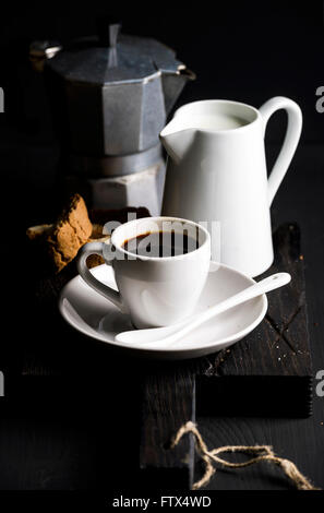 Il caffè italiano set. Tazza di caffè caldo, creamer con latte, cantucci e moka pot su un rustico di legno, sfondo scuro, sel Foto Stock