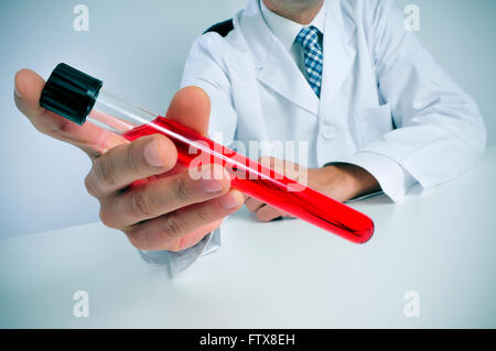 Primo piano di un giovane uomo caucasico indossa mantello bianco seduto alla sua scrivania contiene un campione di sangue in sua mano Foto Stock