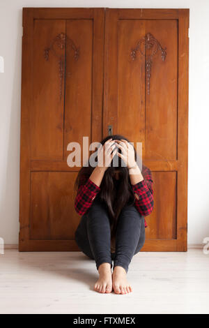 Ragazza seduta sul pavimento con la sua testa con le mani Foto Stock