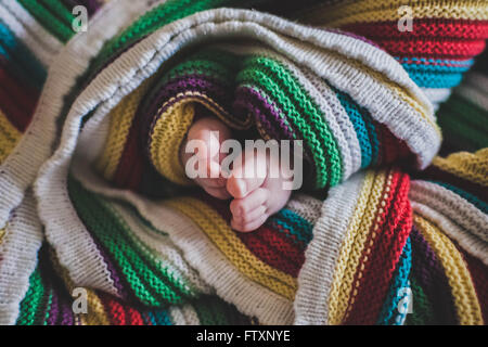 Primo piano dei piedi del bambino avvolti in una coperta multicolore Foto Stock