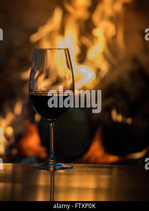 Bicchiere di vino rosso su un tavolo davanti a un caminetto Foto Stock