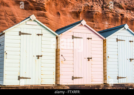 Beach Hut fila in colori pastello, roccia rossa sfondo, South Devon, Regno Unito Foto Stock