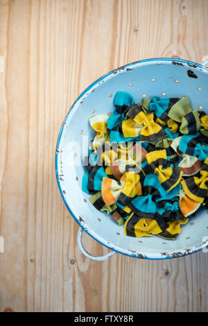 Fantasia di farfalle di pasta. Farfalle di pasta. Aromatizzato pasta colorata. Specialità cucinate la pasta in un blu retrò scolapasta Foto Stock