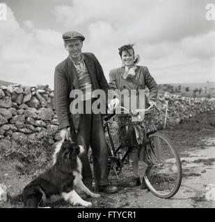 Anni '50, foto storica di J Allan Cash dall'Irlanda occidentale, tutti sorride come agricoltore irlandese con cane da pecora e sua moglie con la sua sosta in bicicletta su una corsia di campagna per la loro foto. Foto Stock