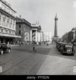 Degli anni Cinquanta, vista storica di O'Connell Street, Dublin, Irlanda con autovetture dell'era parcheggiata e nella distanza "Nelson pilastro dell'. Costruito nel 1809 e noto come il pilastro, è stata una grande colonna di granito coperte da una statua di Orazio Nelson. Foto Stock