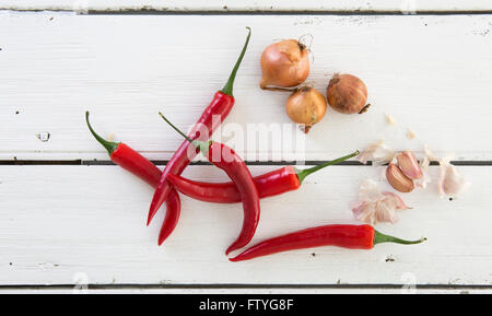 Peperoni rossi con aglio e scalogno su un bianco rustico tavolo in legno Foto Stock