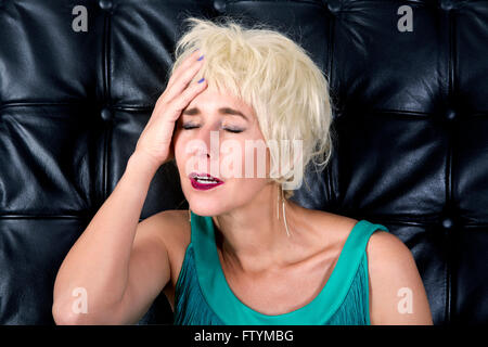 Donna bionda in abito verde con un mal di testa nella parte anteriore del nero parete in pelle Foto Stock