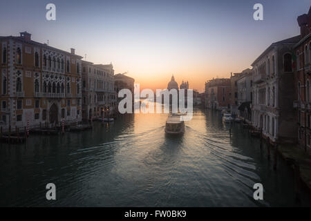 Misty sunrise sul Canal Grande di Venezia con una voce di traghetto verso la Basilica di Santa Maria della Salute Foto Stock