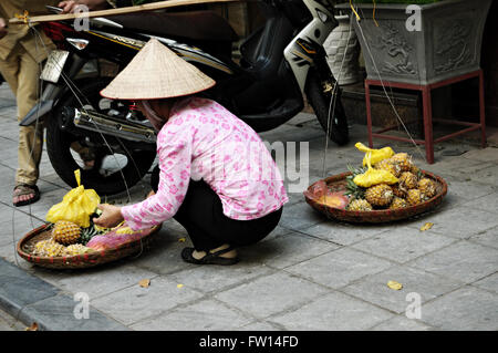 Donna vietnamita con il tipico cappello conico vendita di ananas nel quartiere vecchio di Hanoi, Vietnam Foto Stock