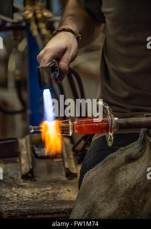 Artigiani di vetro utilizza una torcia a mano per ammorbidire il pezzo egli sta lavorando a. Foto Stock