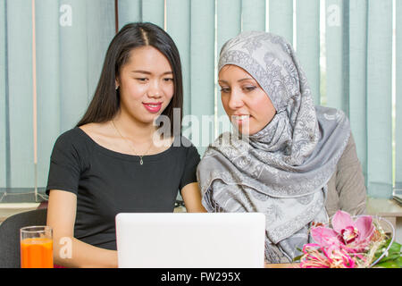 Asiatici e ragazze musulmane che lavorano insieme su un computer portatile Foto Stock