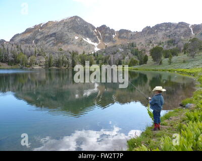 Giovani cowboy di pesca in lago di alta montagna con le montagne sullo sfondo e di riflessione nel lago. Foto Stock