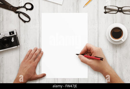 Uomo di scrivere con la penna rossa su isolato, libro bianco. Caffè, bicchieri, fotocamera, notepad matita su un tavolo di legno. Vista dall'alto. Foto Stock