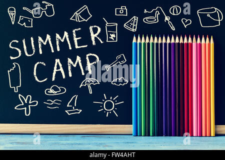 Alcuni disegni di roba estiva e il testo Summer Camp scritto su una lavagna e alcune matite colorate di diversi colori su Foto Stock