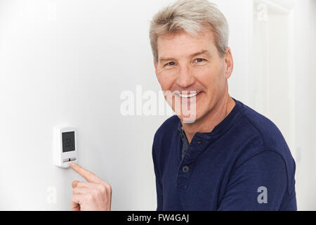 Uomo sorridente termostato di regolazione sulla home del sistema di riscaldamento Foto Stock