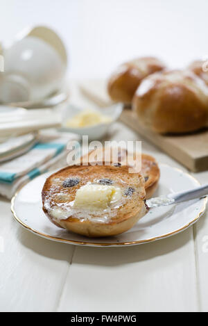 Tostato caldo in casa croce panini con burro di fusione collocato su una crema un tavolo di legno. Foto Stock