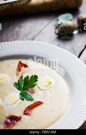 Cremosa Zuppa di rafano con uovo di quaglia, prosciutto della Foresta Nera, decorato con foglie di prezzemolo. La zuppa in un piatto fondo su un grigio scheda di legno Foto Stock