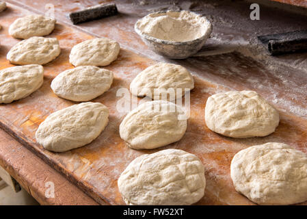 Rendendo il pane fresco in una panetteria con singoli round di porzioni di impasto in piedi pronti per il forno su di un tavolo di legno con una ciotola Foto Stock