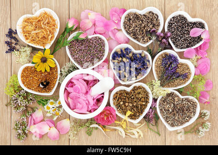 Fiori e erbe selezione medicina usato in alternativa i trattamenti di guarigione nel cuore a forma di tazze in porcellana con mortaio e pestello Foto Stock