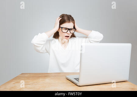 Preoccupato scioccato ragazza adolescente in bicchieri utilizzando laptop tramite grigio Foto Stock