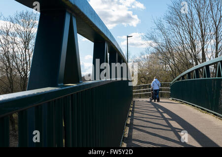 Donna con un passeggino camminare su una passerella sopra la a419 a Cirencester, Gloucestershire, Regno Unito Foto Stock