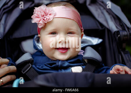 Baby sitting in una carrozzina, tenendo la mia madre del dito, una benda sulla sua testa con un fiore rosa. Baby sorridente e alla ricerca Foto Stock