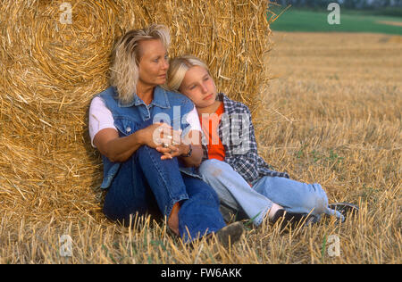 Madre e figlia in un campo appoggiata contro un round per balle di fieno Foto Stock